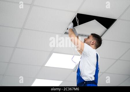 Full Length Portrait Of Electrician On Stepladder Installs Lighting To The Ceiling In Office Stock Photo