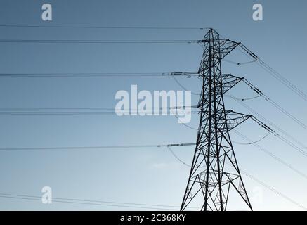 a tall electricity pylon with multiple high voltage cables silhouetted against a blue sky Stock Photo