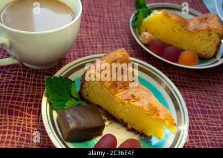 Pie and coffee with milk on a tablecloth burgundy color. A piece of pie with jelly candies and chocolate candi is taken  on a  saucer Stock Photo