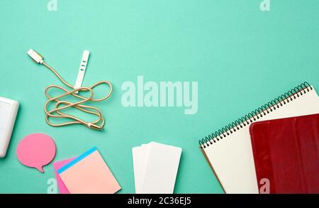 open notebook with blank white sheets, wireless headphones and charger on a green background, top view, copy space Stock Photo