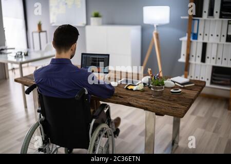 Businessman On Wheelchair While Working On Computer Stock Photo