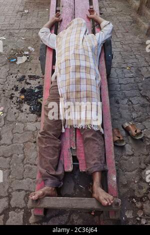 An Indian handcart pusher is sleeping on his long-size cart, face and body covered with a piece of cloth; Kalbadevi Road, Bhuleshwar, Mumbai, India Stock Photo