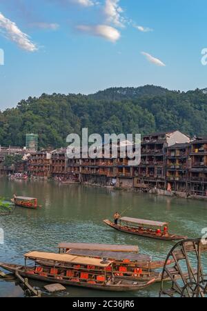 Feng Huang, China -  August 2019 : Old historic wooden tourist boats on the riverbanks of Tuo river, flowing through the centre of Fenghuang Old Town Stock Photo