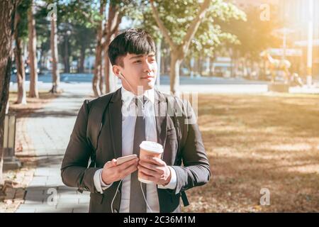 Businessman holding mobile phone while walking on street to office Stock Photo