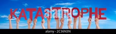People Hands Holding Colorful German Word Katastrophe Means Catastrophe. Blue Sky As Background Stock Photo