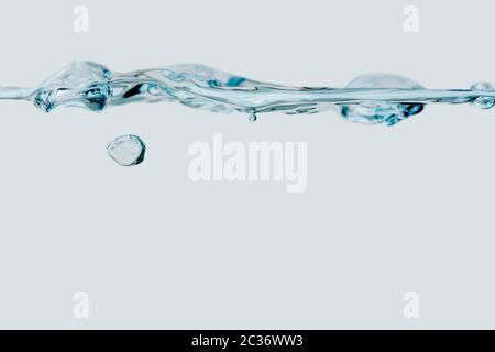 Studio shot of a small water wave with a single rising bubble against white background. Stock Photo