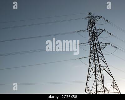 a tall electricity pylon with multiple high voltage cables silhouetted against a blue sky