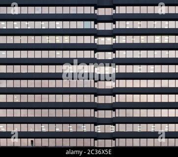 the facade of a large office urban building with rows of windows illuminated at twilight Stock Photo