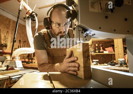 portrait of a carpenter inside his carpentry workshop using a band saw. Wear ear and eye protection Stock Photo
