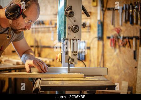 portrait of a carpenter inside his carpentry workshop using a band saw. Wear ear and eye protection Stock Photo
