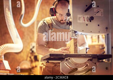 portrait of a carpenter inside his carpentry workshop using a band saw. Wear ear and eye protection Stock Photo