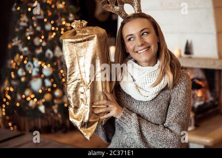 Portrait of a cheerful woman with Christmas gift, beautiful girl enjoying cozy winter eve in the festive decorated house near Christmas tree, Happy Ne Stock Photo