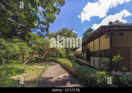 Tea House named Rakuutei lined by a path surrounded by pine trees and stone lantern in Shinjuku Gyoe Stock Photo
