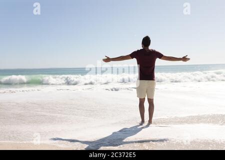 Young mixed race man raising arms on the beach Stock Photo