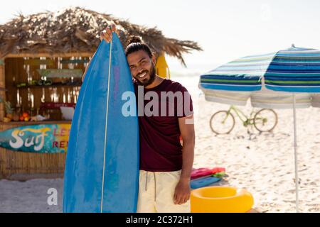 Mixed race man holding surf board on beach Stock Photo