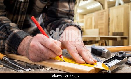 Close-up. Carpenter with pencil and carpenter's square draw the cutting line on a wooden board. Construction industry, carpentry workshop. Stock Photo