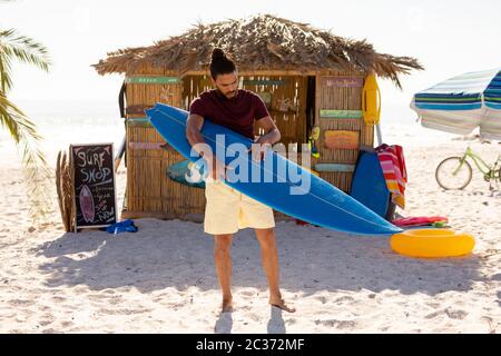 Mixed race man holding surf board on beach Stock Photo