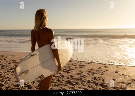 Young caucasian woman holding surf board on beach Stock Photo