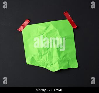 green crumpled sheet of paper glued with rubber red adhesive tape on a black background, copy space Stock Photo