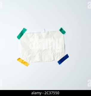white crumpled sheet of paper torn from a spiral notebook and glued with multi-colored electrical tape on a white background, place for text Stock Photo