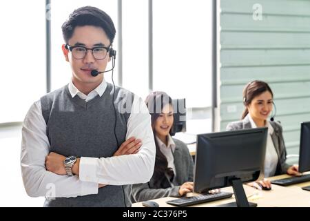 Portrait of Young adult friendly and confidence operator man with headsets and his team working in a call center as customer service and technical sup Stock Photo