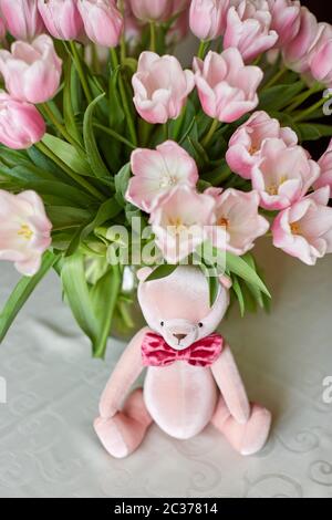 Pink bear toy and a vase with pink tulips on a table. Decor. Selective focus. Stock Photo