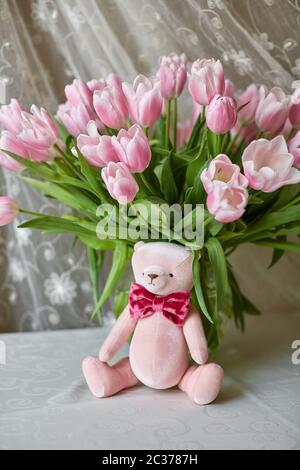Pink bear toy and a vase with pink tulips on a table. Decor. Selective focus. Stock Photo