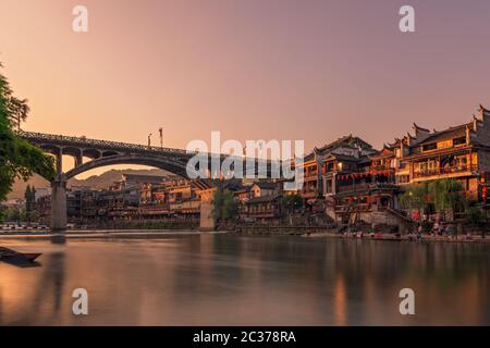 Feng Huang, China -  August 2019 : Long time exposure of the road bridge over Tuo Jiang river and wooden houses in ancient old town of Fenghuang known Stock Photo