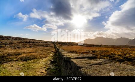 Mourn Wall on the bank of Slieve Donard mountain with blue sky, white clouds and sunrays Stock Photo