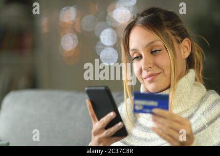 Woman buying on-line in the night with credit card sitting on a couch in the night at home in winter Stock Photo
