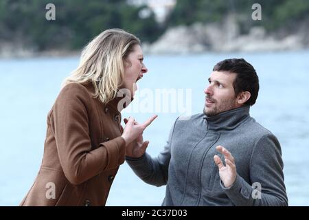Angry woman shouting to her scared husband on the beach Stock Photo