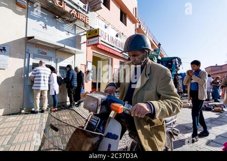 Marrakech, Morocco, Feb 2019: Old muslim man wearing helmet, driving old motorbike, scooter on crowded street in Moroccan old town medina Stock Photo