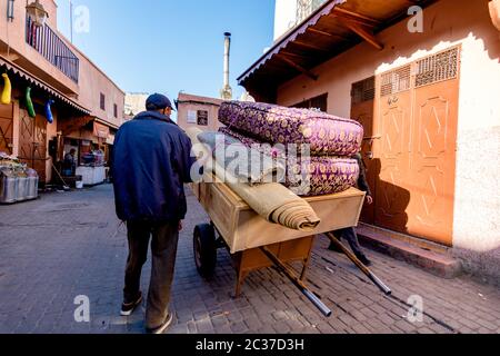 Marrakech, Morocco, Feb 2019: Old muslim man with cart selling carpets at traditional oriental bazaar, street market in Morocco. Moroccan old town Stock Photo