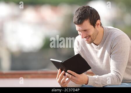 Happy man reading an ebook sitting in a balcony outdoors in a rural town Stock Photo