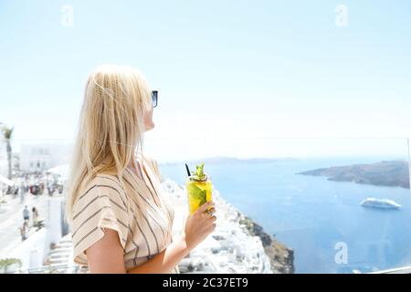 Woman holding a glass of passion fruit cocktail in Santorini background Stock Photo