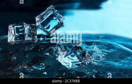 Ice cubes falling into the blue water. Splash of ice water. Water splashes from falling ice cubes. Stock Photo