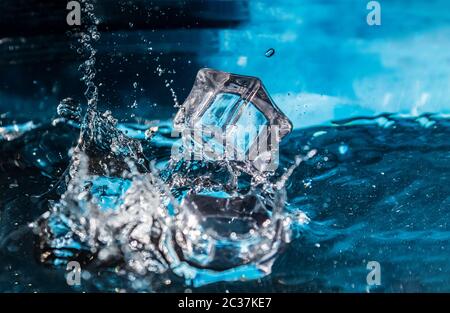 Ice cubes falling into the blue water. Splash of ice water. Water splashes from falling ice cubes. Stock Photo