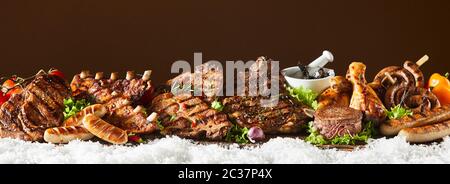 Panorama banner with large selection of barbecued meat including sausage, beef, pork, spare ribs, chicken on a bed of salad greens on winter snow with Stock Photo