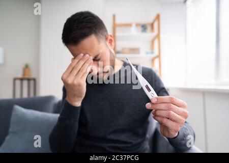 Sick Man Holding With Fever Holding Thermometer Showing High Temperature Stock Photo