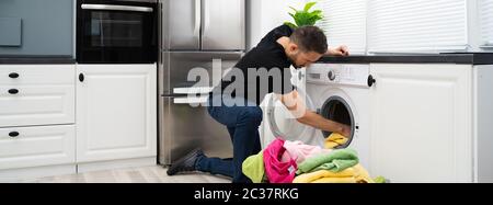 Man Loading Clothes Into Washing Machine In Kitchen Stock Photo