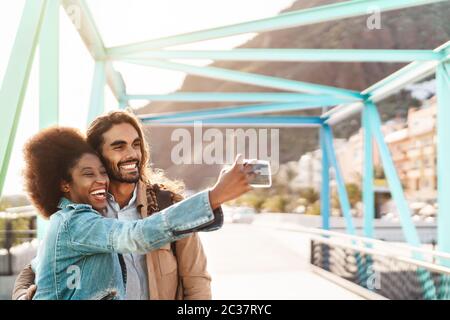Happy smiling couple taking selfie with mobile smartphone outdoor - Young trendy people having fun during vacations Stock Photo