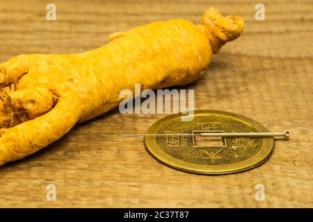 Acupuncture needle on Chinese coin with ginseng root Stock Photo