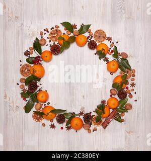 Festive frame from ripe mandarins with leaves, nuts, spices on light wooden background. Top view with copy space. Stock Photo