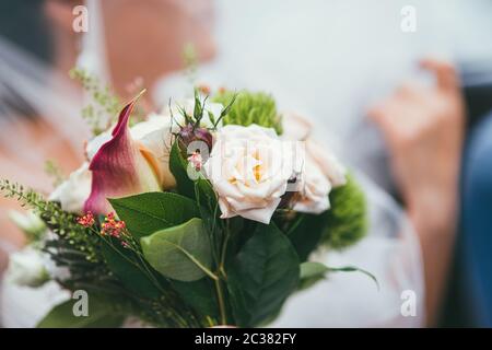 Beautiful wedding bouquet of the bride with delicate roses on the background of the blurred veil and the bride's hand. Selective Stock Photo