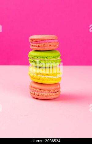 Multi-colored macaroons stand in a pile on a pink table. Close-up Stock Photo