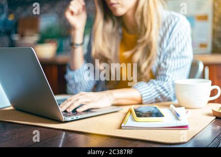 Home office woman and distance learning online education. Cropped beautiful lady girl working at notebook in kitchen and drinking coffee at home