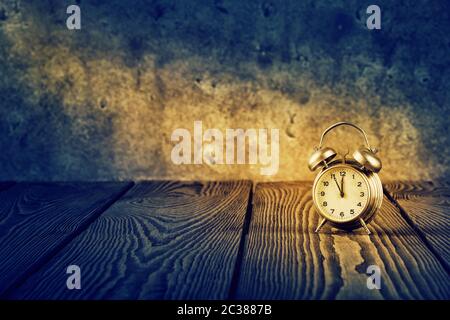 Old alarm clock under beam of light on wooden table Stock Photo