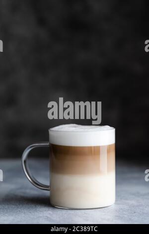 Cafe latte macchiato layered coffee in a a glass mug, vertical shot with dark  gray background and room for text at the top. Stock Photo