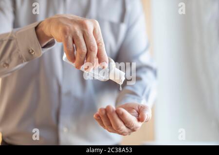 Close up of alcohol gel sanitizer pushed out of a bottle in the hands of a man wearing a blue shirt. Selective focus. Copy space. Stock Photo