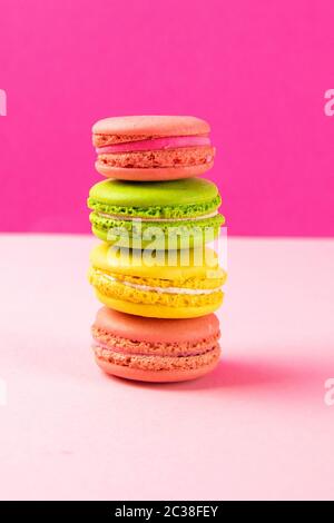Multi-colored macaroons stand in a pile on a pink table. Close-up Stock Photo
